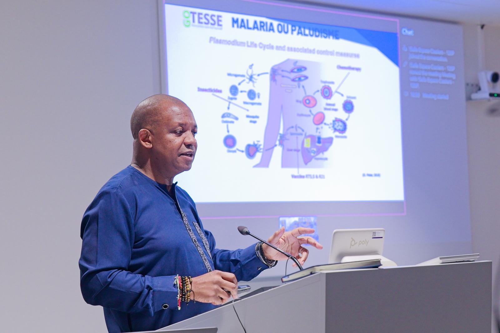 Le Pr Jean Cyr Yombi en conférence devant un schéma du cycle du paludisme, logo Gotesse