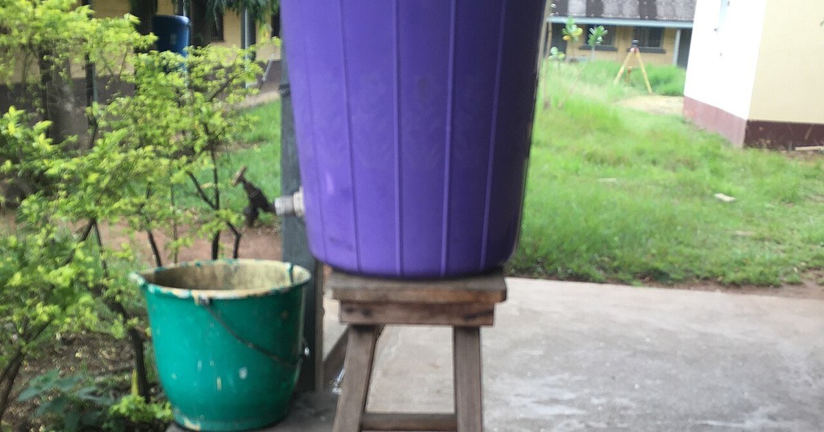 Dispositif de lavage des mains en Afrique de l'Ouest : seau violet à robinet posé sur un tabouret en bois et seau de récupération