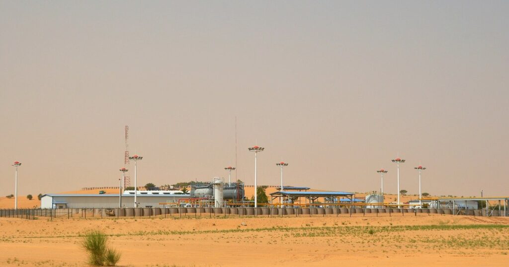 Installations pétrolières de CNPC-Niger dans le bloc d'Agadem, au milieu des dunes de la région de Diffa : réservoirs, séparateurs, tuyauteries jaunes et mâts d'éclairage derrière une clôture