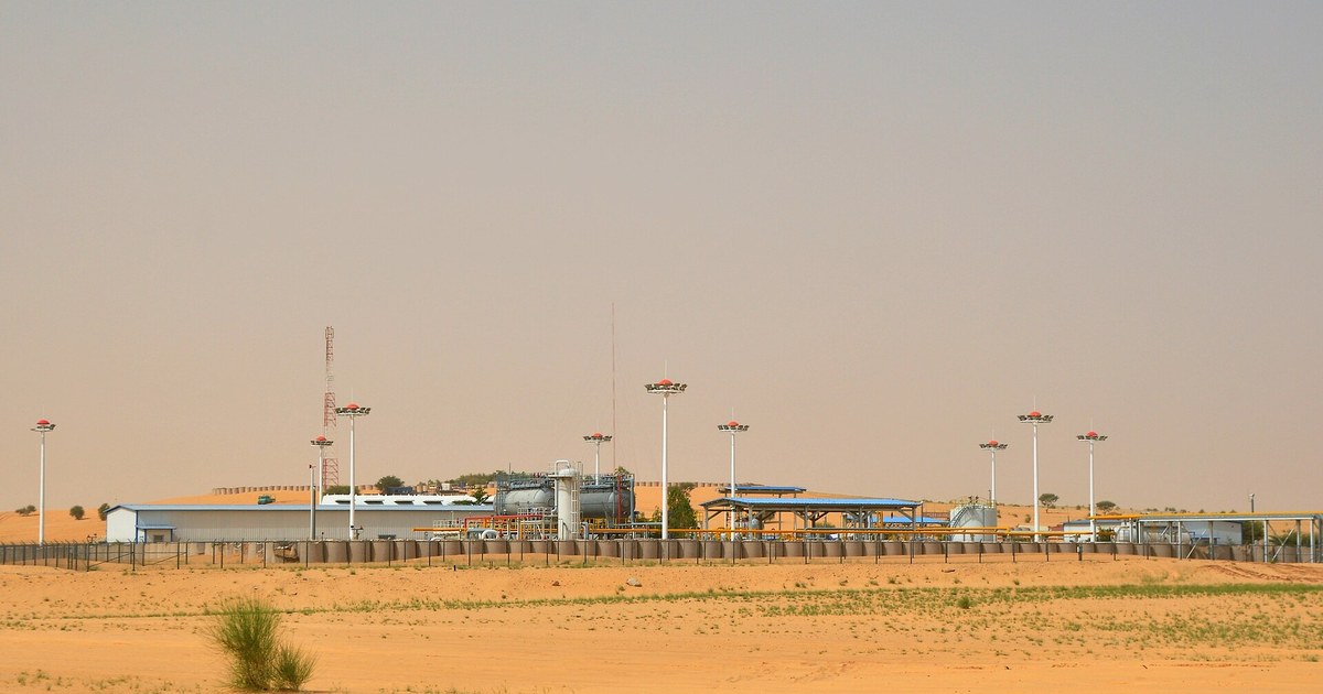 Installations pétrolières de CNPC-Niger dans le bloc d'Agadem, au milieu des dunes de la région de Diffa : réservoirs, séparateurs, tuyauteries jaunes et mâts d'éclairage derrière une clôture