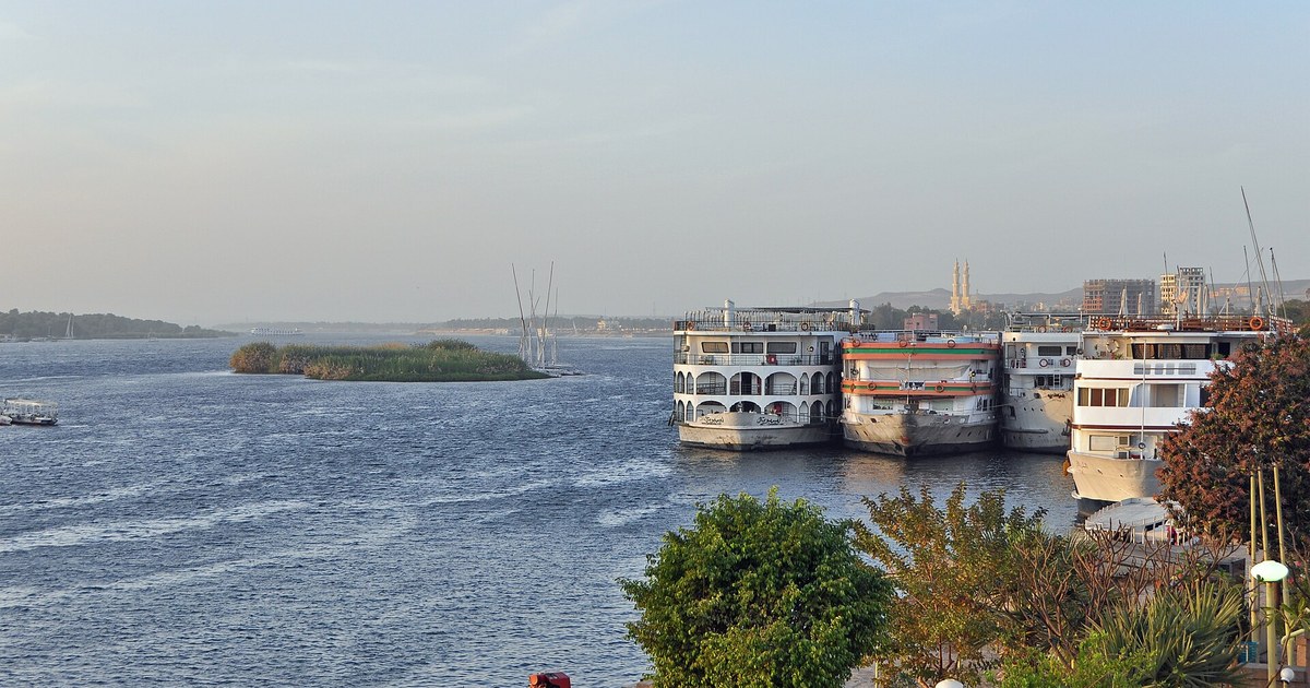 Le Nil à Assouan, en Égypte, avec bateaux de croisière à quai et une pompe sur la berge, fleuve au cœur de l'accord du bassin du Nil