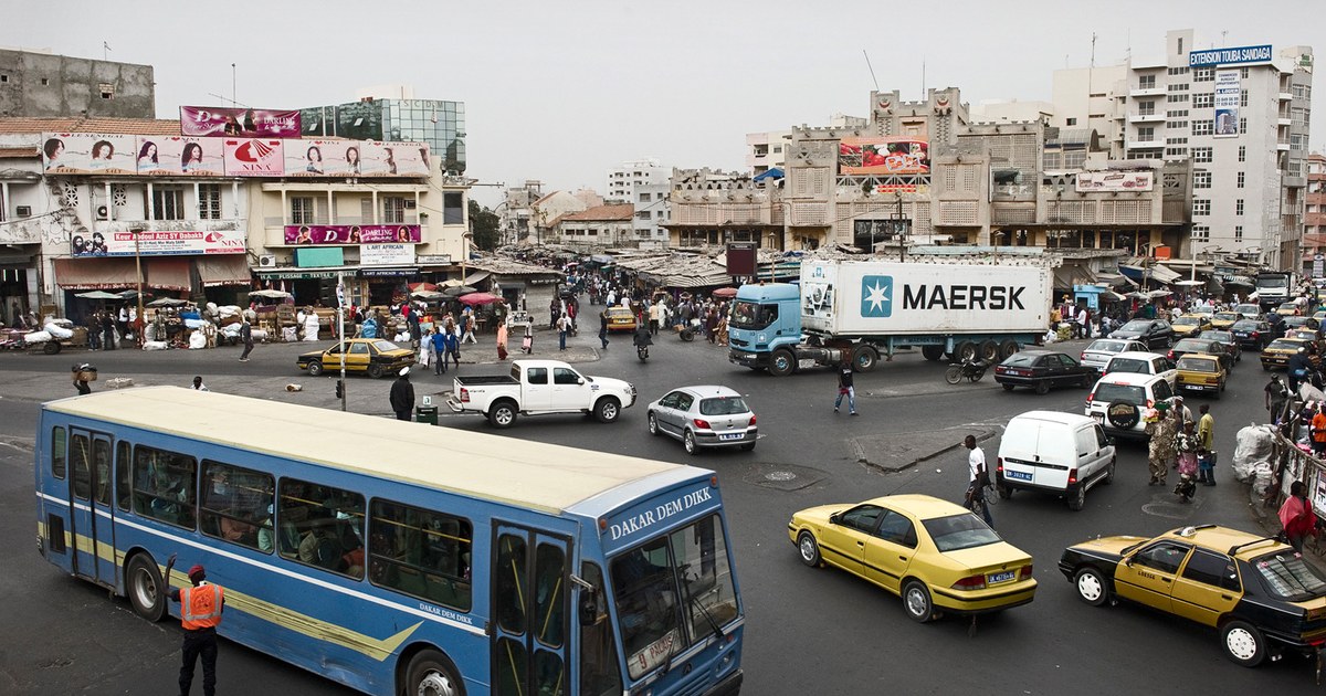 Carrefour commerçant animé à Dakar, avec un bus Dakar Dem Dikk, des taxis jaunes et des boutiques, en illustration des fonds envoyés par la diaspora sénégalaise